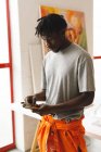 Pintor afroamericano en el trabajo sosteniendo pinceles en el estudio de arte. creación e inspiración en un estudio de pintura de artistas. - foto de stock