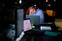 Homme d'affaires métis travaillant la nuit, assis au bureau et utilisant un ordinateur portable. travailler tard dans les affaires dans un bureau moderne. — Photo de stock