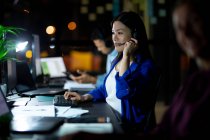 Mujer de negocios asiática que trabaja de noche con auriculares. trabajar hasta tarde en los negocios en una oficina moderna. - foto de stock