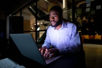 Empresário afro-americano trabalhando à noite, sentado à mesa e usando laptop. trabalhando até tarde em negócios em um escritório moderno. — Fotografia de Stock