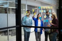 Divers collègues d'affaires masculins et féminins lisant des notes de service colorées sur un mur de verre. travailler en entreprise dans un bureau moderne. — Photo de stock