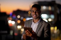 Retrato de hombre de negocios de raza mixta trabajando por la noche usando tableta. trabajar hasta tarde en los negocios en una oficina moderna. - foto de stock