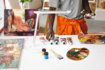 Pintor afro-americano no trabalho segurando tintas no estúdio de arte. criação e inspiração em um estúdio de pintura de artistas. — Fotografia de Stock