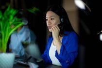 Mulher de negócios asiática trabalhando à noite usando fone de ouvido. trabalhando até tarde em negócios em um escritório moderno. — Fotografia de Stock
