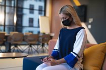 Mujer de negocios caucásica que usa mascarilla y teléfono inteligente. trabajando en negocios en una oficina moderna durante la pandemia de coronavirus covid 19. - foto de stock