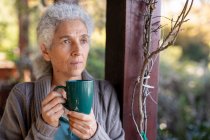 Расслабляющая пожилая кавказка на балконе стоит и пьет кофе. пенсионного образа жизни, проводить время в одиночестве на дому. — стоковое фото