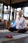 Senior caucasian woman in living room exercising, sitting on the floor and meditating. retirement lifestyle, spending time alone at home. — Stock Photo