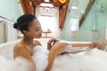 Femme de race mixte dans la salle de bain ayant une baignoire et se rasant les jambes. mode de vie domestique, profiter de loisirs d'auto-soins à la maison. — Photo de stock