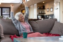 Heureuse femme caucasienne âgée assise sur le canapé et utilisant une tablette dans le salon moderne. mode de vie à la retraite, passer du temps seul à la maison. — Photo de stock