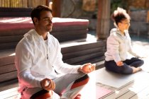 Разнообразная пара в спортивной одежде и практикующая йогу на коврике для йоги. проводить свободное время дома. — стоковое фото