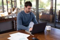 Caucasian man sitting at table and working remotely using laptop. working at home in modern apartment. — Stock Photo