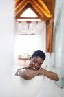 Retrato de mujer afroamericana sonriente en el baño, relajante en el baño. estilo de vida doméstico, disfrutando del tiempo libre de autocuidado en casa. - foto de stock