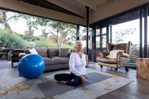 Mujer caucásica mayor en la sala de estar haciendo ejercicio, sentado en el suelo. estilo de vida de jubilación, pasar tiempo solo en casa. - foto de stock