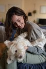 Lächelnde Kaukasierin im Wohnzimmer, die auf dem Sofa sitzt und ihren Hund umarmt. häuslicher Lebensstil, Freizeit zu Hause genießen. — Stockfoto