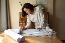 Кавказька жінка-архітектор у вітальні, сидячи за столом і малюючи плани. Домашній спосіб життя, дистанційна праця з дому. — стокове фото