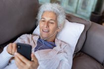 Eine ältere kaukasische Frau liegt im modernen Wohnzimmer und benutzt ihr Smartphone. Lebensstil im Ruhestand, Zeit allein zu Hause verbringen. — Stockfoto