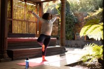 Смешанная расовая женщина носит спортивную одежду и практикует йогу на коврике для йоги. проводить свободное время дома. — стоковое фото