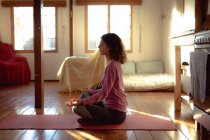 Donna razza mista praticare yoga, seduto meditando in soggiorno soleggiato. stile di vita sano, godendo del tempo libero a casa. — Foto stock