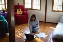 Mujer de raza mixta que trabaja a distancia utilizando el ordenador portátil en la sala de estar soleada. estilo de vida saludable, trabajo remoto desde casa. - foto de stock