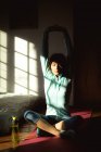 Смешанная расовая женщина практикует йогу, растягиваясь в солнечной гостиной. здоровый образ жизни, наслаждаясь отдыхом дома. — стоковое фото