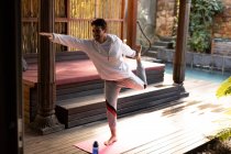 Uomo caucasico che indossa abbigliamento sportivo e pratica yoga in piedi su tappetino yoga. trascorrere del tempo libero a casa. — Foto stock
