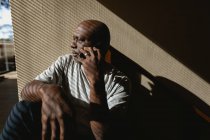 Homme afro-américain senior assis dans les escaliers et parlant sur le smartphone. mode de vie à la retraite, passer du temps seul à la maison. — Photo de stock
