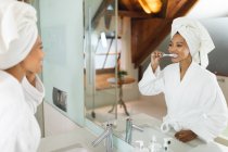 Расовая женщина в ванной с зубной щеткой в руках, чистит зубы. домашний образ жизни, наслаждаясь отдыхом на дому. — стоковое фото