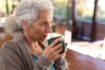 Розслаблююча старша біла жінка на кухні сидить і п'є каву. пенсійний спосіб життя, проводити час наодинці вдома . — стокове фото