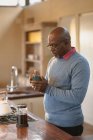 Homme afro-américain senior debout dans la cuisine moderne en buvant un café. mode de vie à la retraite, passer du temps seul à la maison. — Photo de stock