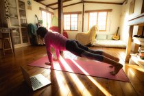 Femme de race mixte pratiquant le yoga, faisant des pompes dans le salon ensoleillé. mode de vie sain, profiter de loisirs à la maison. — Photo de stock