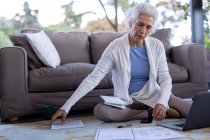 Senior caucasian woman in living room sitting on the floor and using laptop. retirement lifestyle, spending time alone at home. — Stock Photo