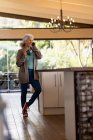 Mulher caucasiana sênior na cozinha usando smartphone e beber café. estilo de vida aposentadoria, passar o tempo sozinho em casa. — Fotografia de Stock