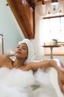 Змішана расова жінка у ванній кімнаті приймає ванну, розслабляючись із закритими очима. домашній спосіб життя, насолоджуючись доглядом за дозвіллям вдома . — стокове фото