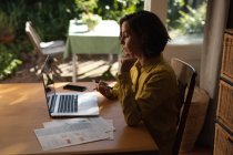 Кавказька жінка у вітальні, сидячи за столом, за допомогою ноутбука. Домашній спосіб життя, дистанційна праця з дому. . — стокове фото