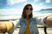 Femme mixte prenant selfie avec smartphone par jour ensoleillé au bord de la mer. mode de vie sain, profiter du temps libre à l'extérieur. — Photo de stock
