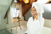 3mixed race femme dans la salle de bain tenant brosse à dents se brossant les dents. mode de vie domestique, profiter de loisirs d'auto-soins à la maison. — Photo de stock