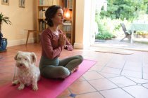 Mulher branca na sala de estar com seu cão de estimação, praticando ioga, meditando. estilo de vida doméstico, desfrutando de tempo de lazer em casa. — Fotografia de Stock