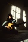 Жінка змішаної раси грає на гітарі в сонячній спальні. здоровий спосіб життя, насолоджуючись дозвіллям вдома . — стокове фото