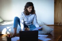 Mixed race woman working remotely using laptop in sunny bedroom. healthy lifestyle, remote working from home. — Stock Photo