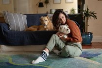 Lächelnde Kaukasierin im Wohnzimmer, die auf dem Boden sitzt und ihren Hund umarmt. häuslicher Lebensstil, Freizeit zu Hause genießen. — Stockfoto