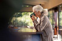 Розслаблююча старша біла жінка на кухні сидить і п'є каву. пенсійний спосіб життя, проводити час наодинці вдома . — стокове фото
