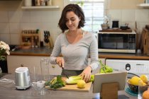 Caucasian woman in kitchen, preparing health drink, chopping vegetables. domestic lifestyle, enjoying leisure time at home. — Stock Photo
