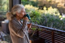Relajante mujer caucásica en el balcón bebiendo café. estilo de vida de jubilación, pasar tiempo solo en casa. - foto de stock