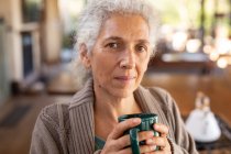 Entspannte ältere Kaukasierin in der Küche stehend und Kaffee trinkend. Lebensstil im Ruhestand, Zeit allein zu Hause verbringen. — Stockfoto