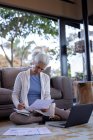 Старша біла жінка у вітальні сидить на підлозі і працює. пенсійний спосіб життя, проводити час наодинці вдома . — стокове фото
