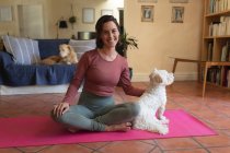 Retrato de mujer caucásica sonriente en salón con sus perros de compañía, practicando yoga. estilo de vida doméstico, disfrutando del tiempo libre en casa. - foto de stock