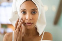 Donna razza mista in bagno applicare la crema viso per la cura della pelle. stile di vita domestico, godendo di auto cura del tempo libero a casa. — Foto stock