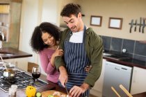 Feliz pareja diversa en la cocina preparando la comida juntos picando verduras. pasar tiempo libre en casa en apartamento moderno. - foto de stock