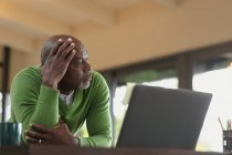 Задумчивый старший африканский американец на современной кухне, работающий над ноутбуком. пенсионного образа жизни, проводить время в одиночестве на дому. — стоковое фото