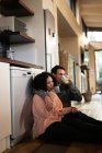 Happy diverse couple in kitchen sitting on floor and drinking coffee. spending time off at home in modern apartment. — Stock Photo